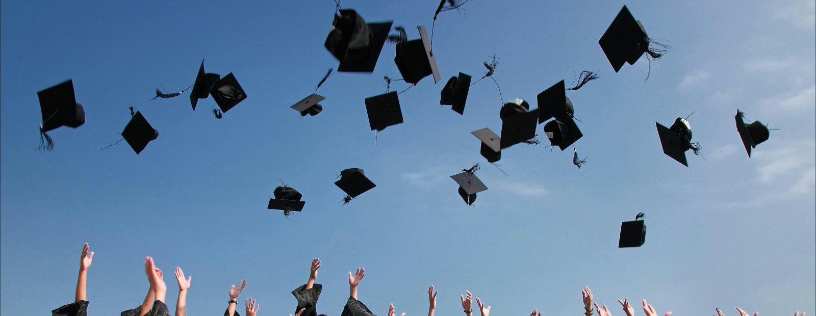 hands throwing mortorboard caps into blue sky 