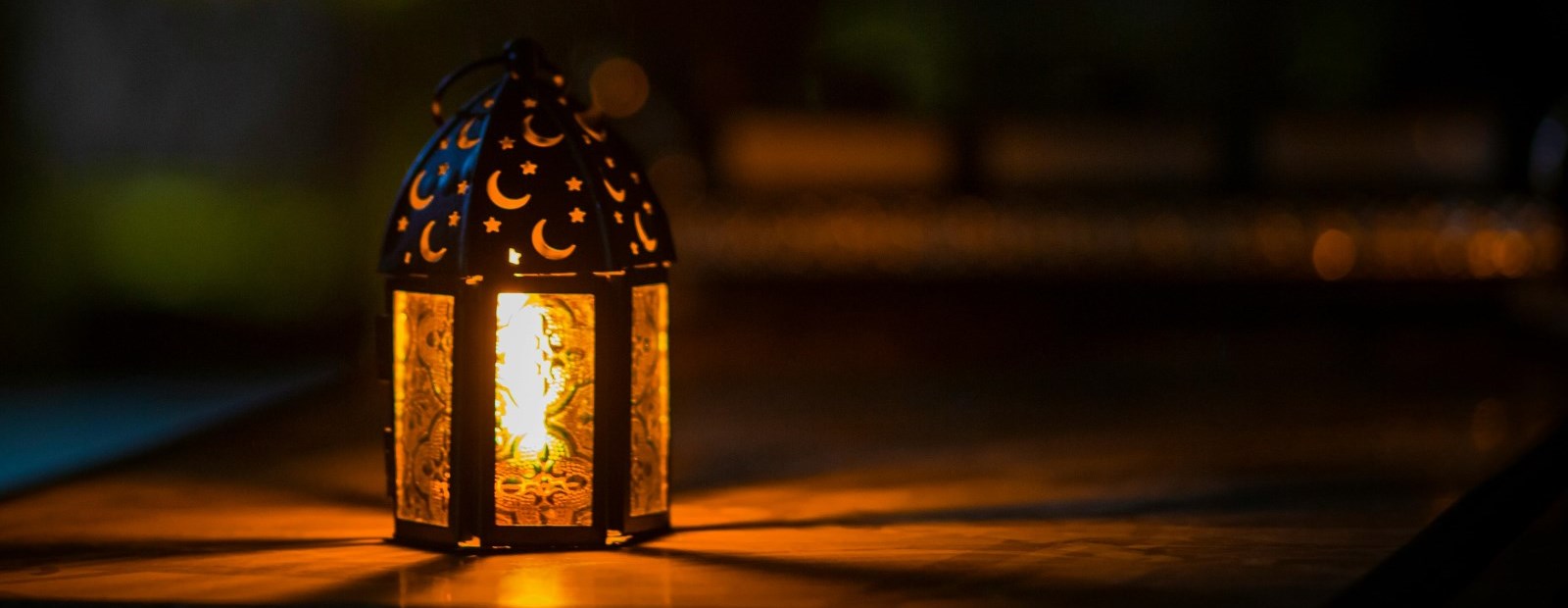 Small lantern with crescent moons shining bright yellow in a dark room.